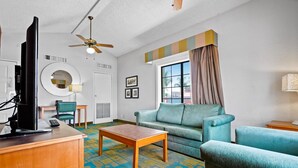 A living room with a sofa, armchair, coffee table, TV, and ceiling fan. - La Quinta Inn by Wyndham Costa Mesa / Newport Beach (Costa Mesa)