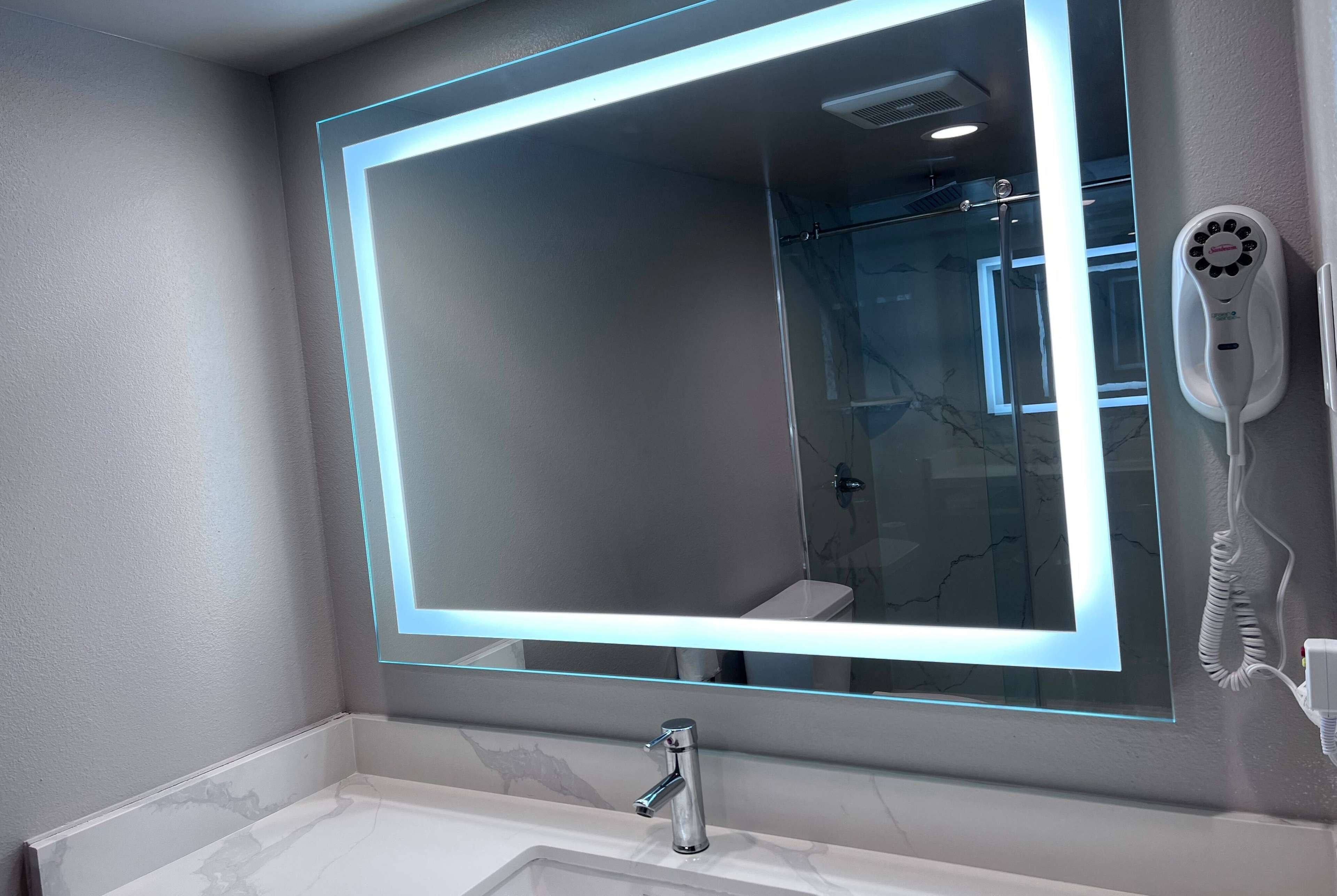 A bathroom with a large mirror, a modern faucet, and a hairdryer mounted on the wall.