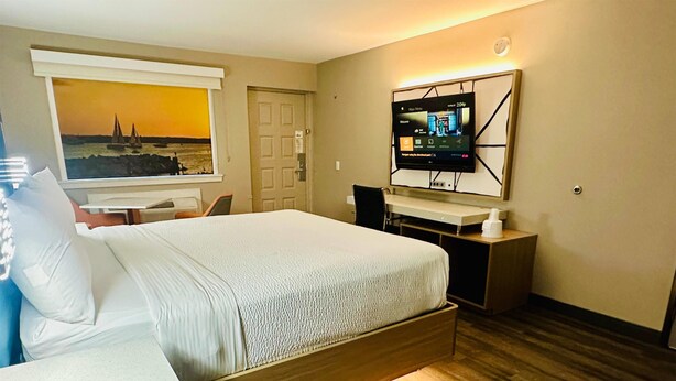 A hotel room with a bed, a desk, a chair, a TV mounted on the wall, and a window with a painting. - La Quinta Inn by Wyndham Costa Mesa / Newport Beach (Costa Mesa)