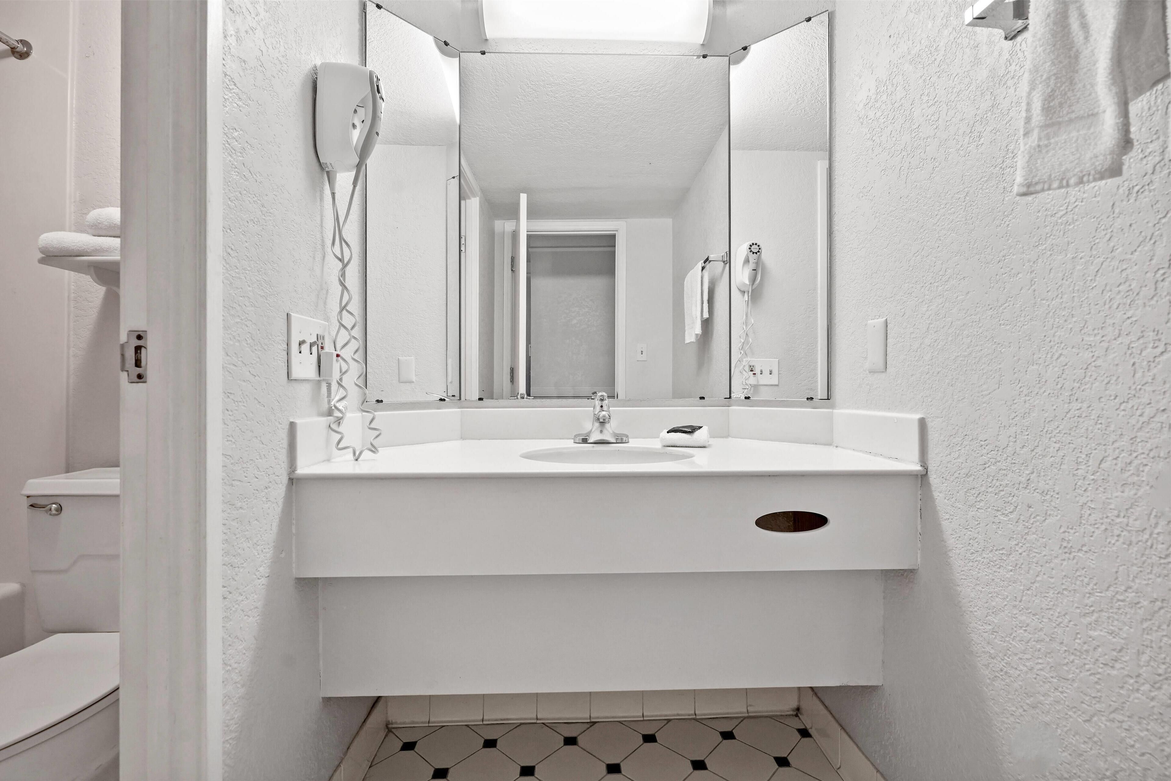 Une salle de bain avec un lavabo blanc, un miroir, un sèche-cheveux et un porte-serviettes.