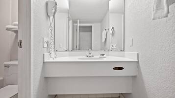 Une salle de bain avec un lavabo blanc, un miroir, un sèche-cheveux et un porte-serviettes.
