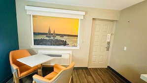 A room with a window overlooking a harbor, a white table, two orange chairs, and a door. - La Quinta Inn by Wyndham Costa Mesa / Newport Beach (Costa Mesa)