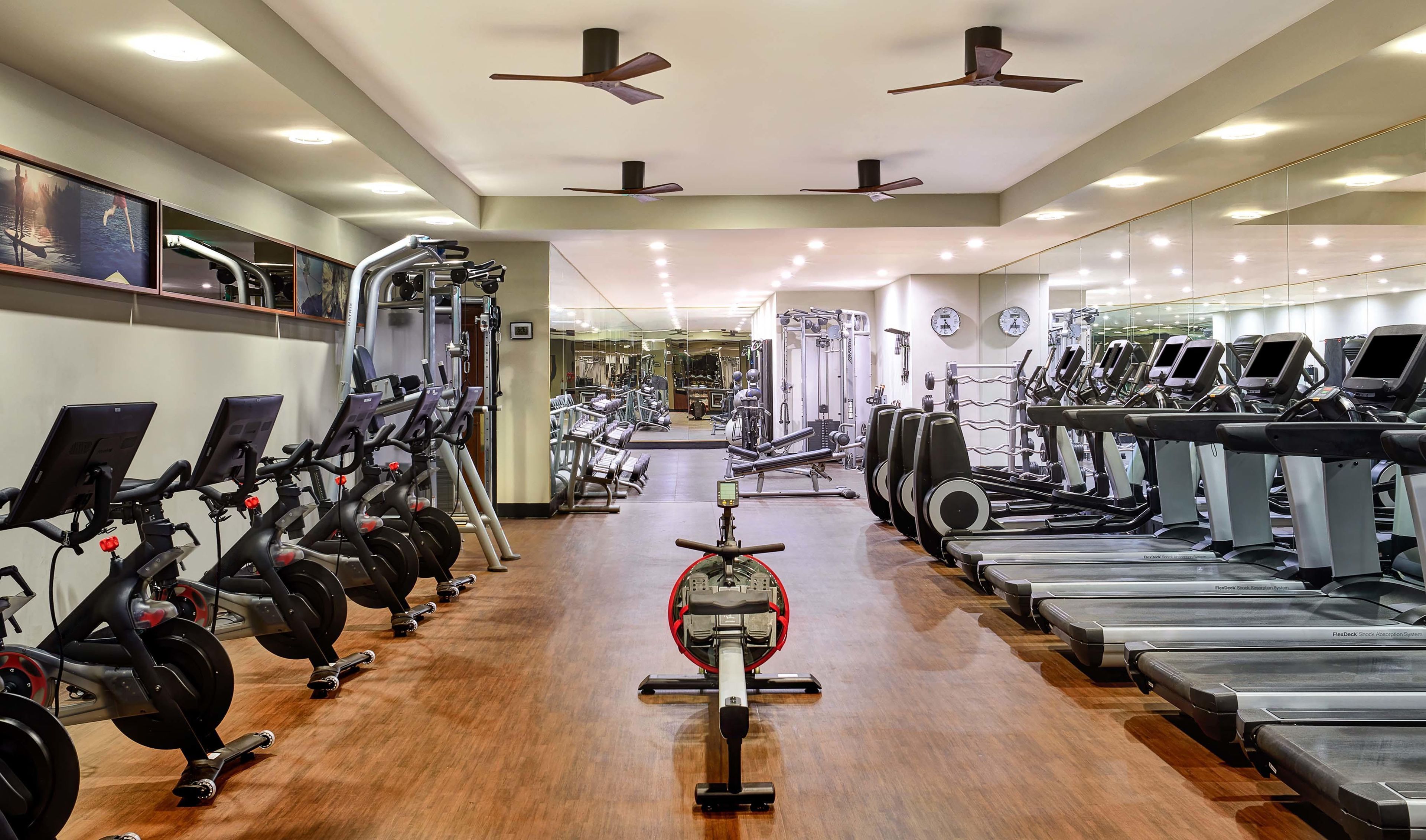 A gym with multiple exercise machines, including treadmills and stationary bikes, arranged in rows.