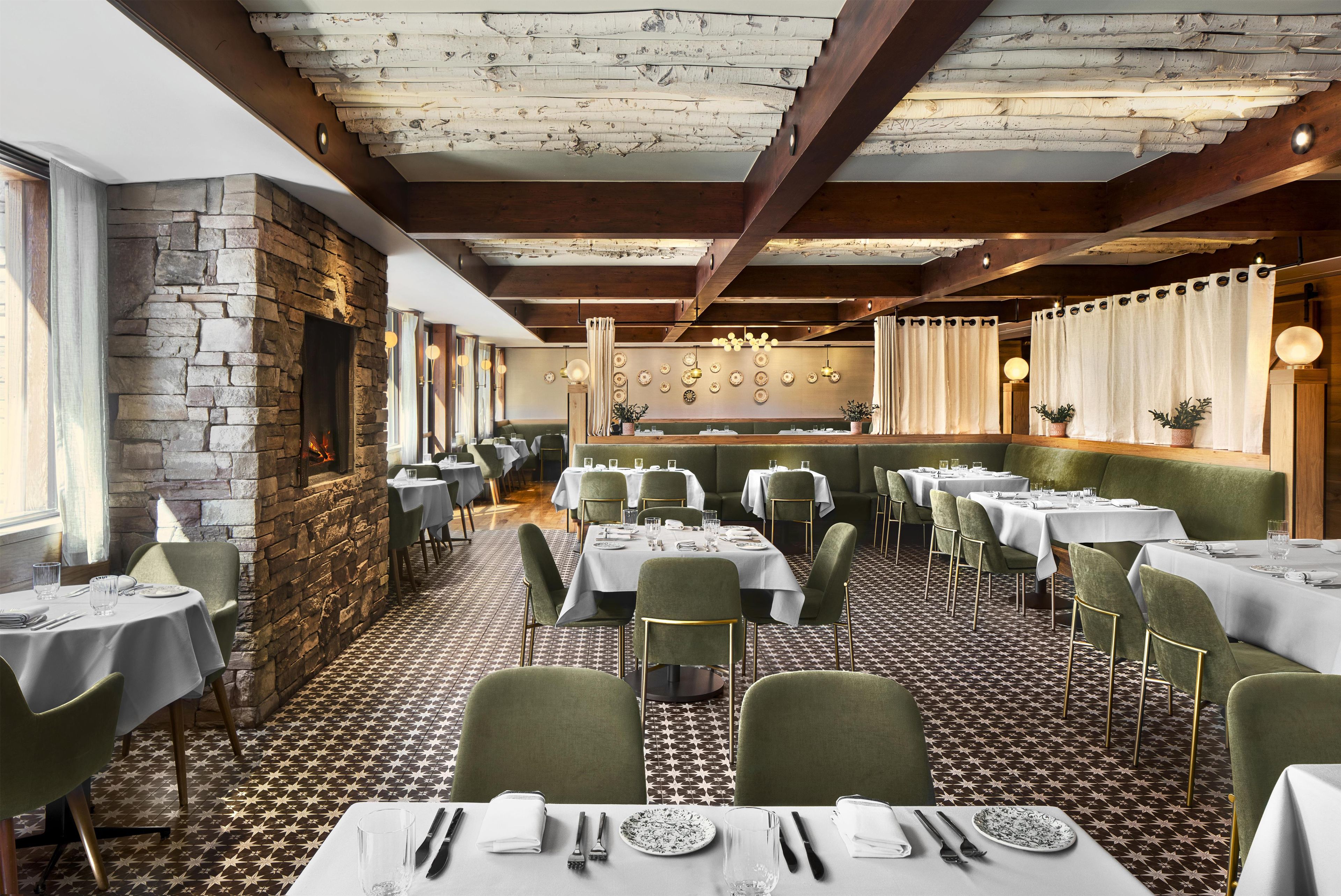 A restaurant with a stone fireplace, green upholstered chairs, and patterned flooring.