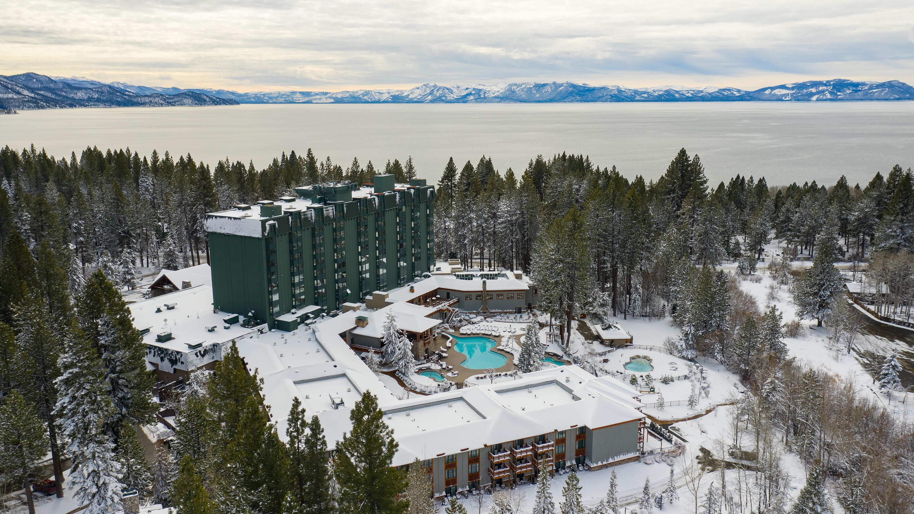 A resort with multiple buildings, a swimming pool, and a view of a lake and mountains.