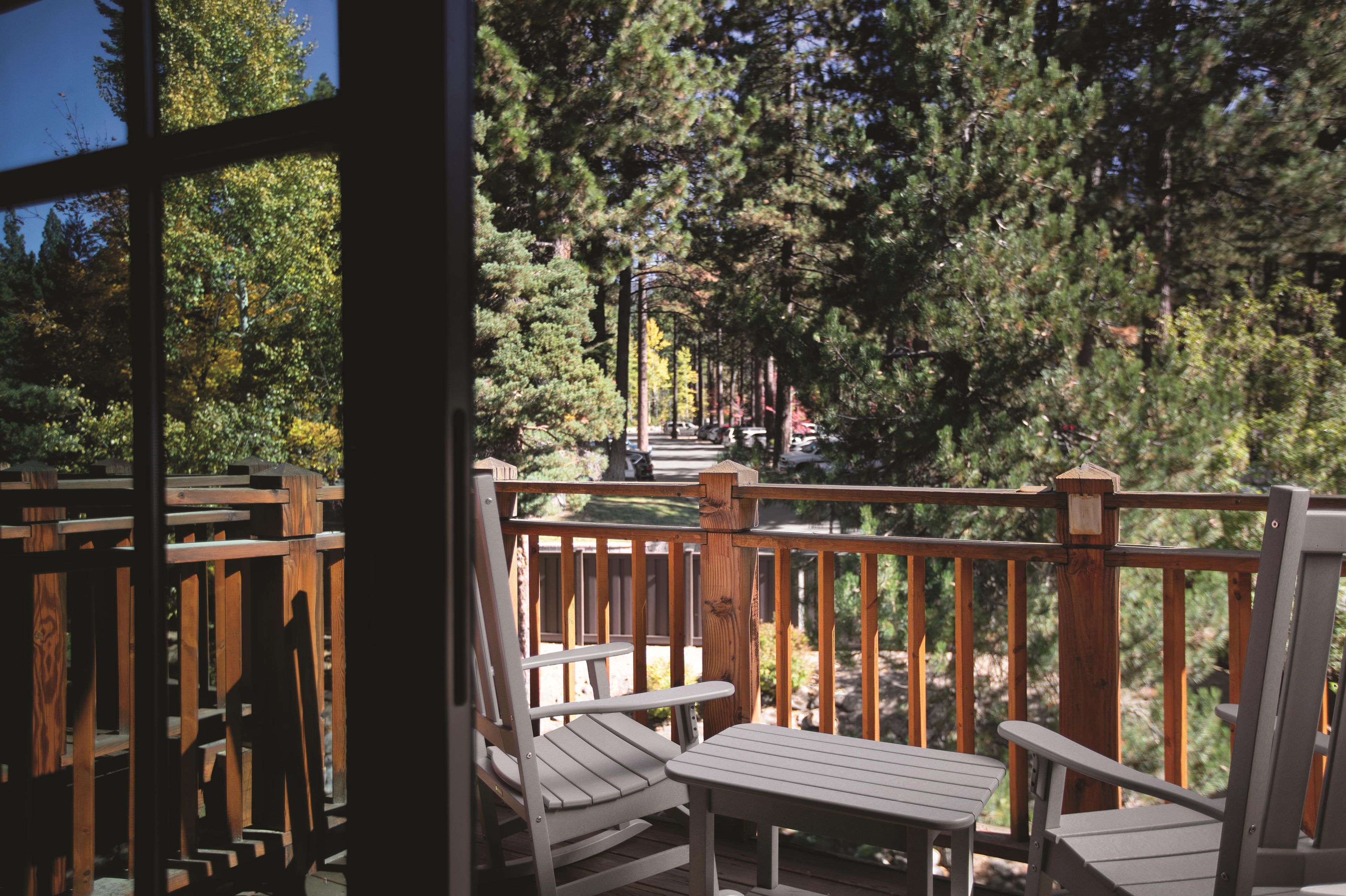 A wooden deck with two chairs and a table, overlooking a forested area.