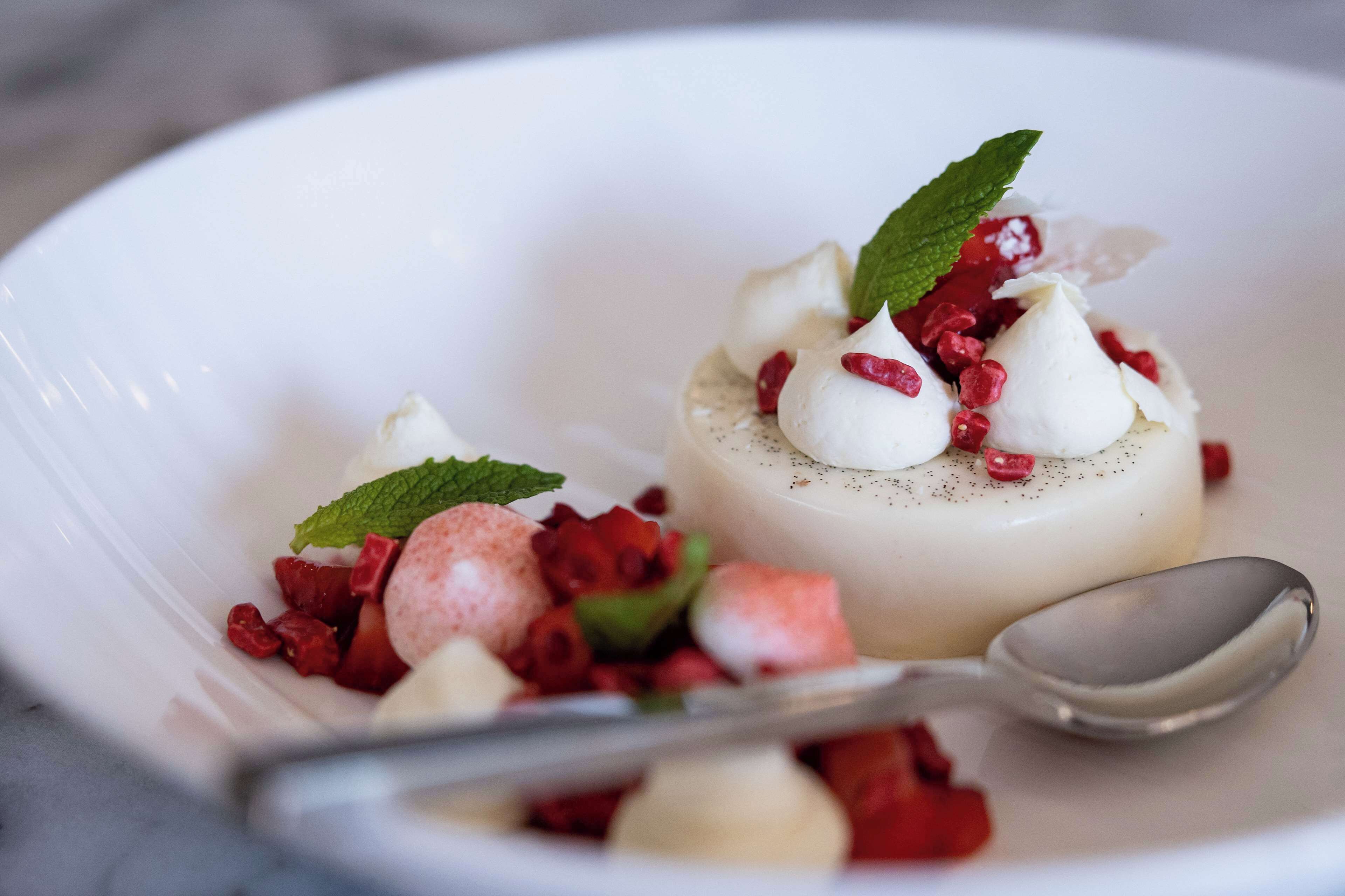 Un dessert composé de crème blanche et de fruits rouges, présenté sur une assiette blanche.