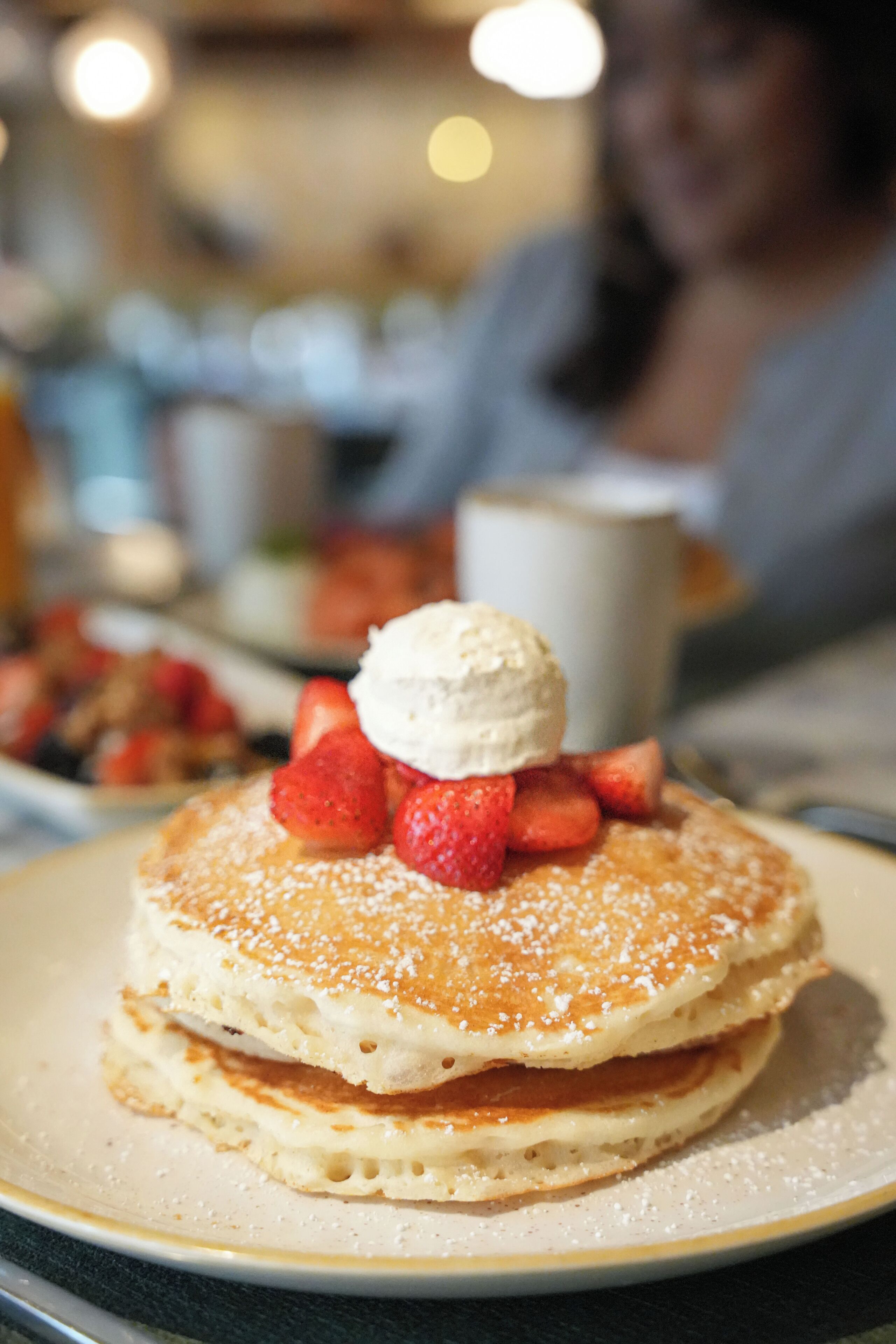 A stack of pancakes with strawberries and a scoop of ice cream on a plate.