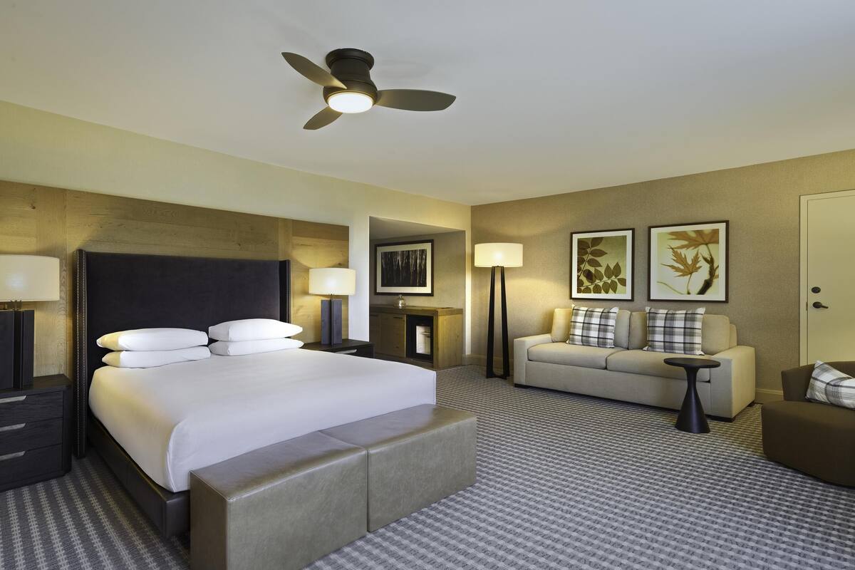 A hotel room with a bed, a sofa, a coffee table, and a ceiling fan.