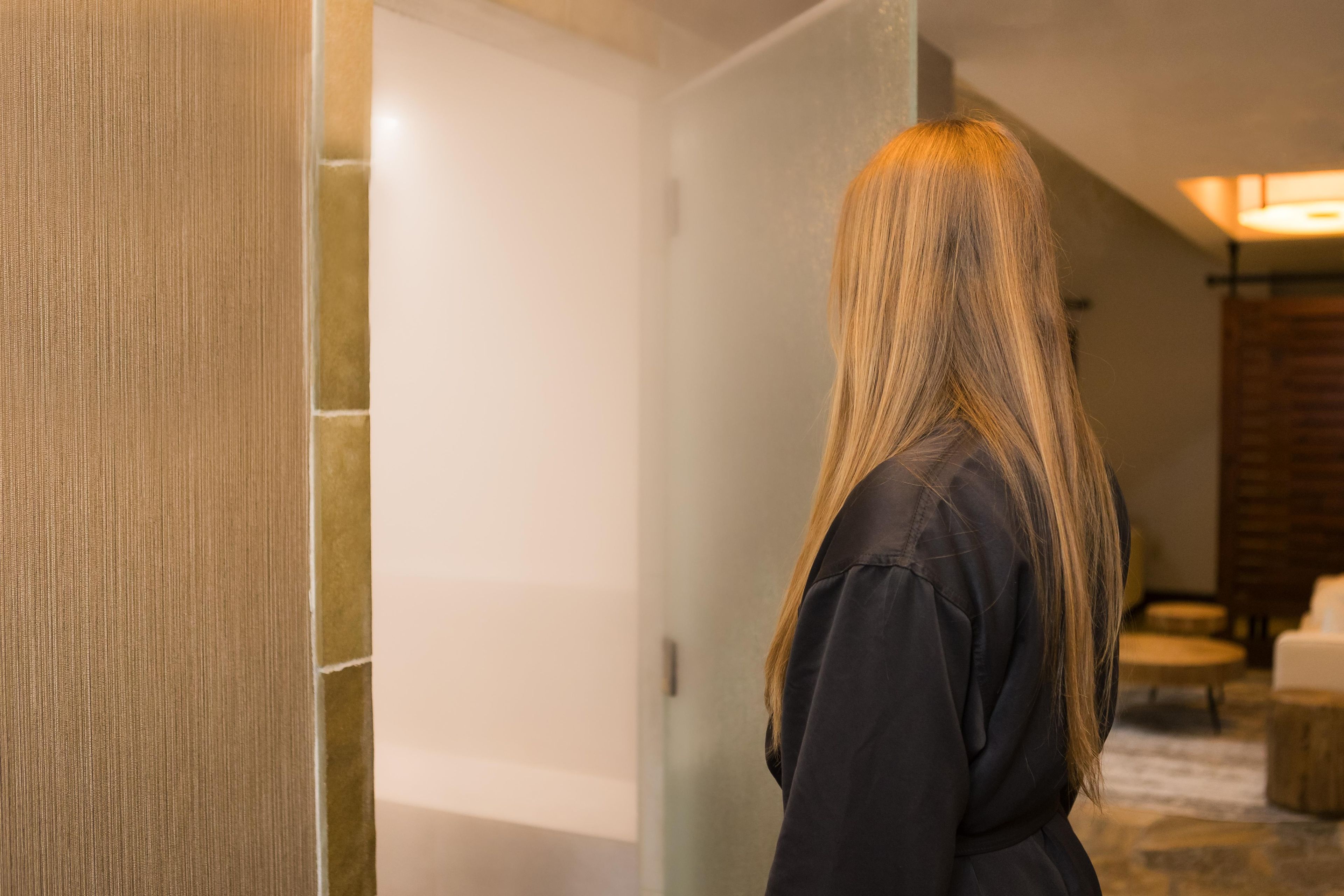 A person standing in a hallway with a textured wall and a door.