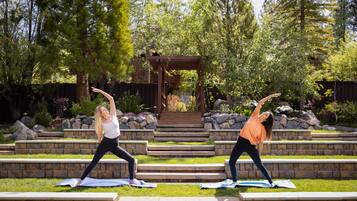 Two people performing yoga on a set of outdoor stairs surrounded by greenery and a wooden pergola.