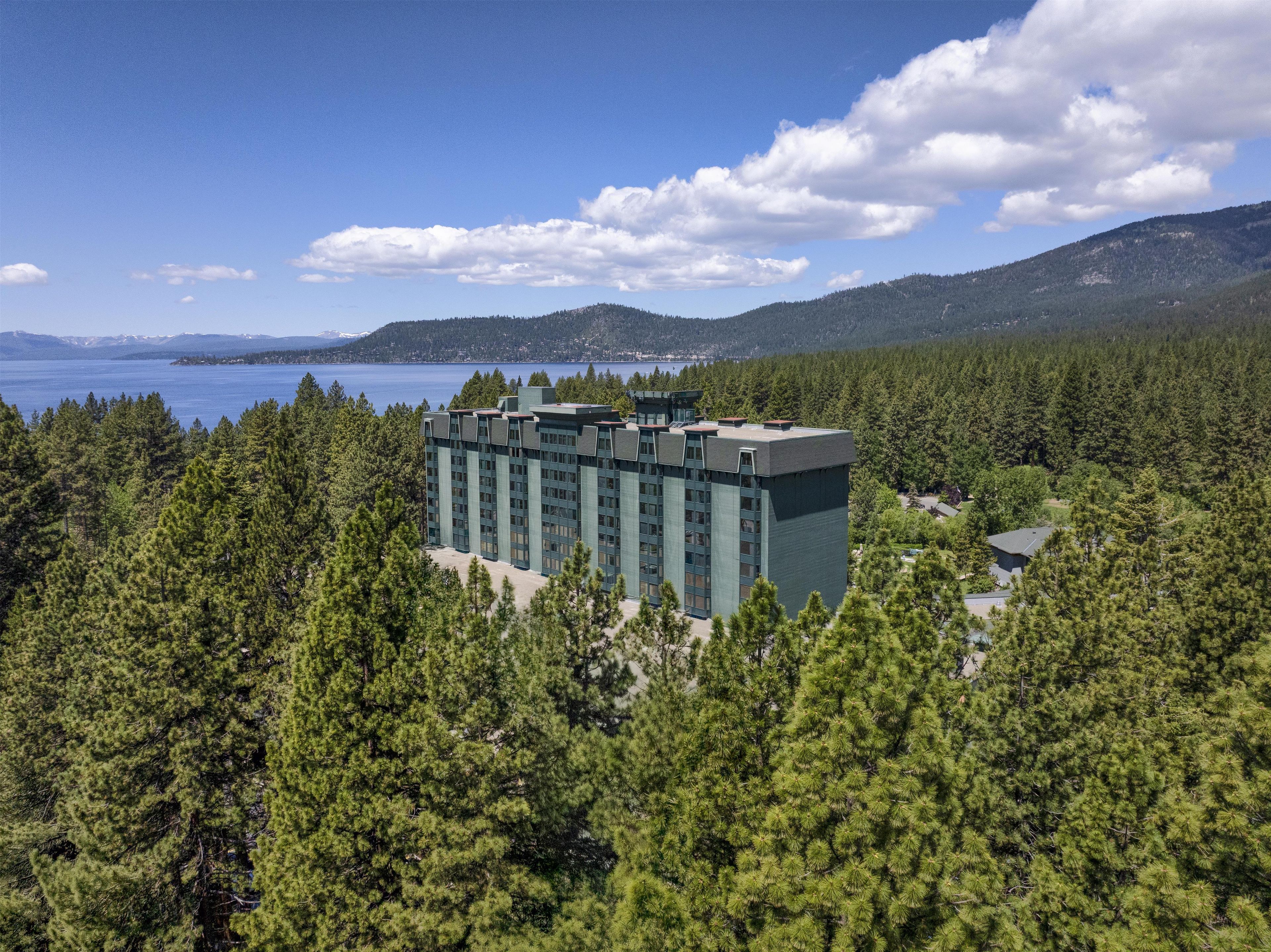 Un hôtel moderne doté d’un toit plat, entouré d’une forêt dense et offrant une vue sur un lac et des montagnes.