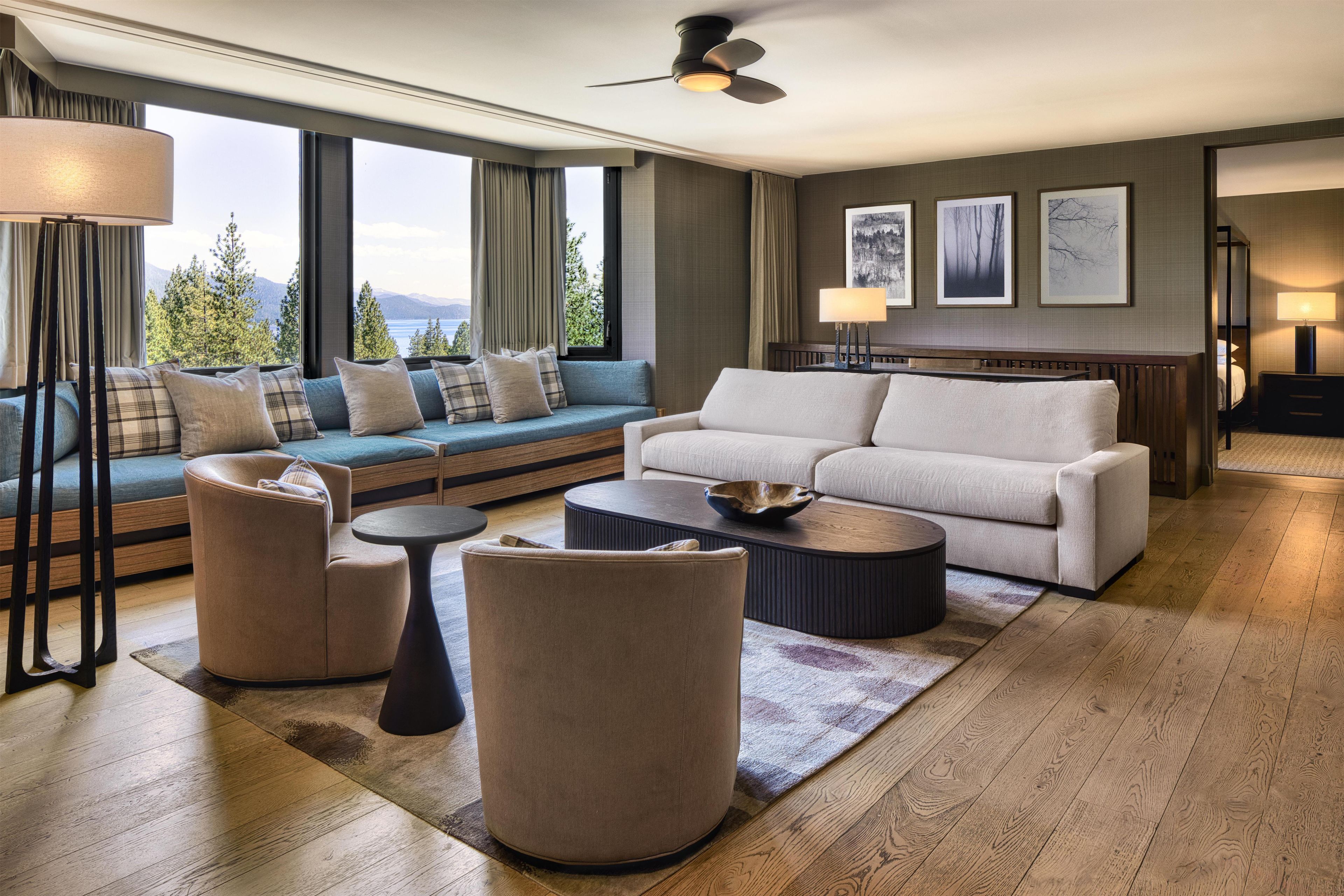 A modern living room with a sofa, armchairs, a coffee table, and a view of mountains through large windows.