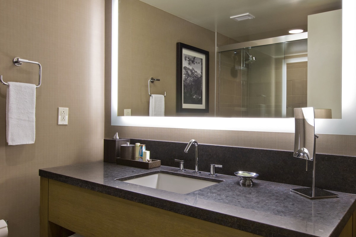 A modern bathroom with a large mirror, two sinks, and wooden shelves holding towels.