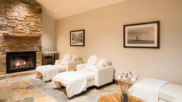 A spa-like room with a stone fireplace, two white sofas, and a wooden coffee table with a vase of dried flowers.