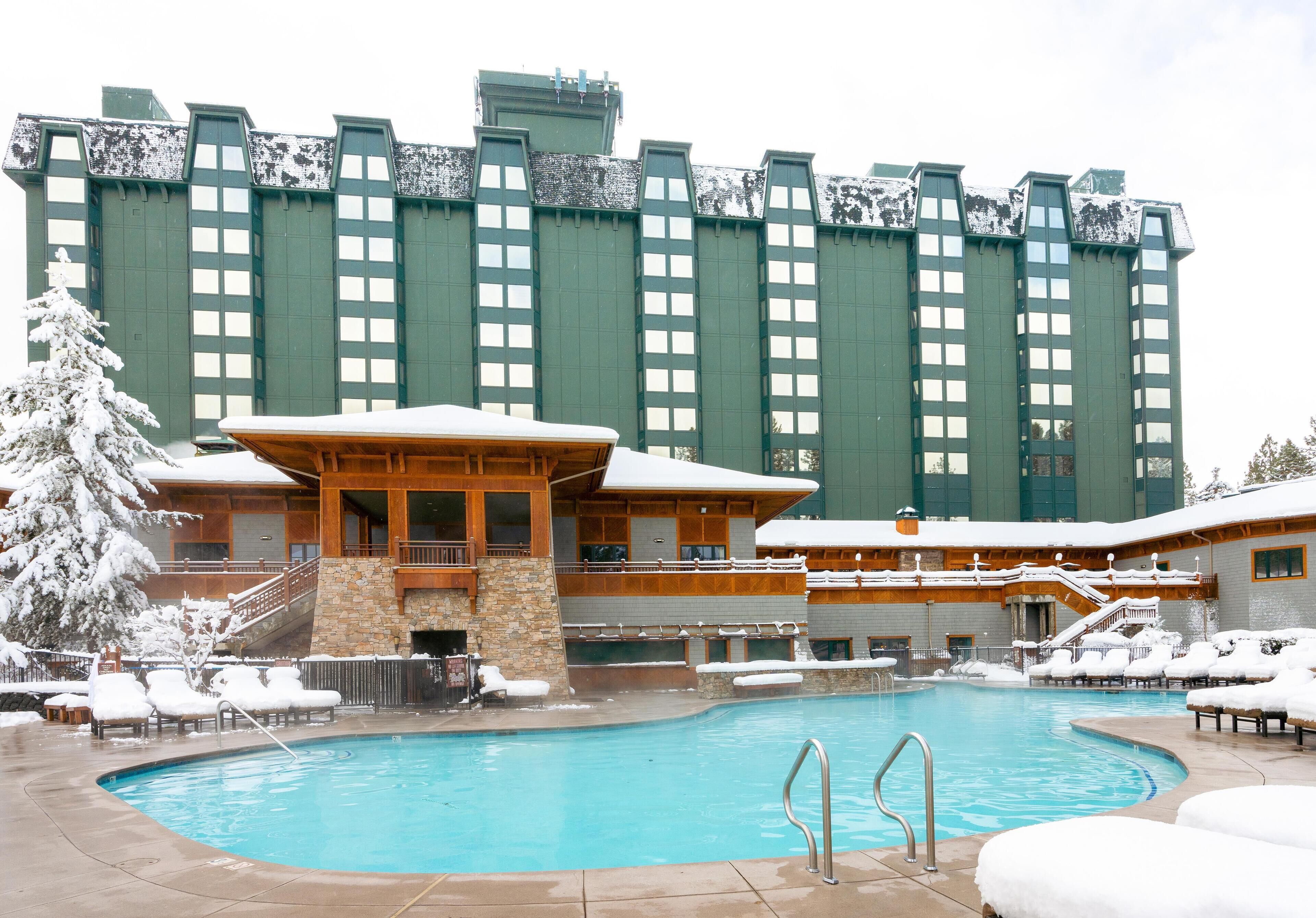 A hotel with a large pool surrounded by lounge chairs and a snow-covered landscape.