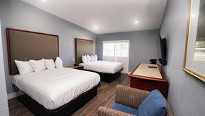 A hotel room with two beds, a desk, a chair, and a television.