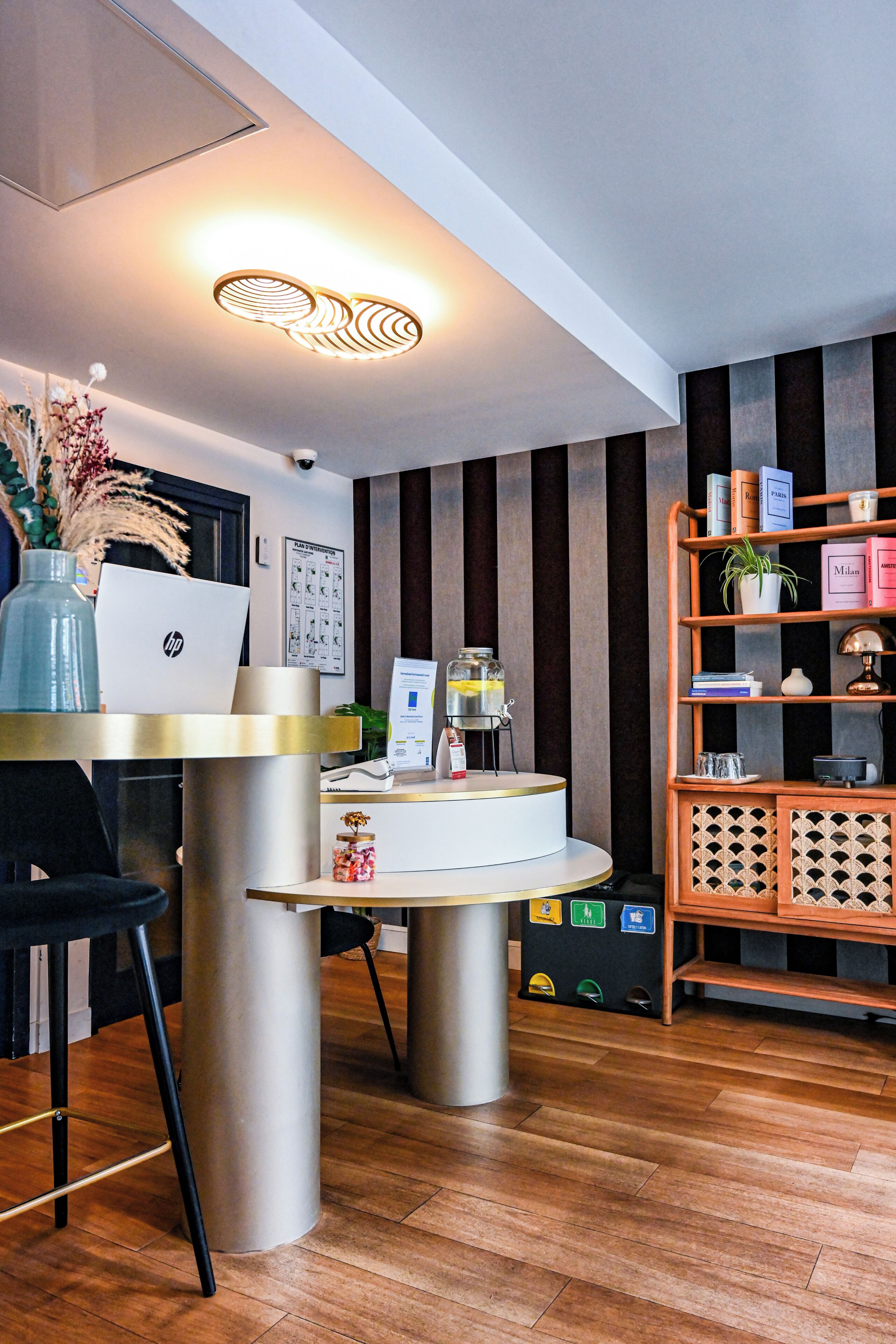 Un comptoir d’accueil avec un ordinateur portable, un vase contenant des fleurs séchées, un tableau d’affichage et une bibliothèque en bois où sont exposés divers objets.