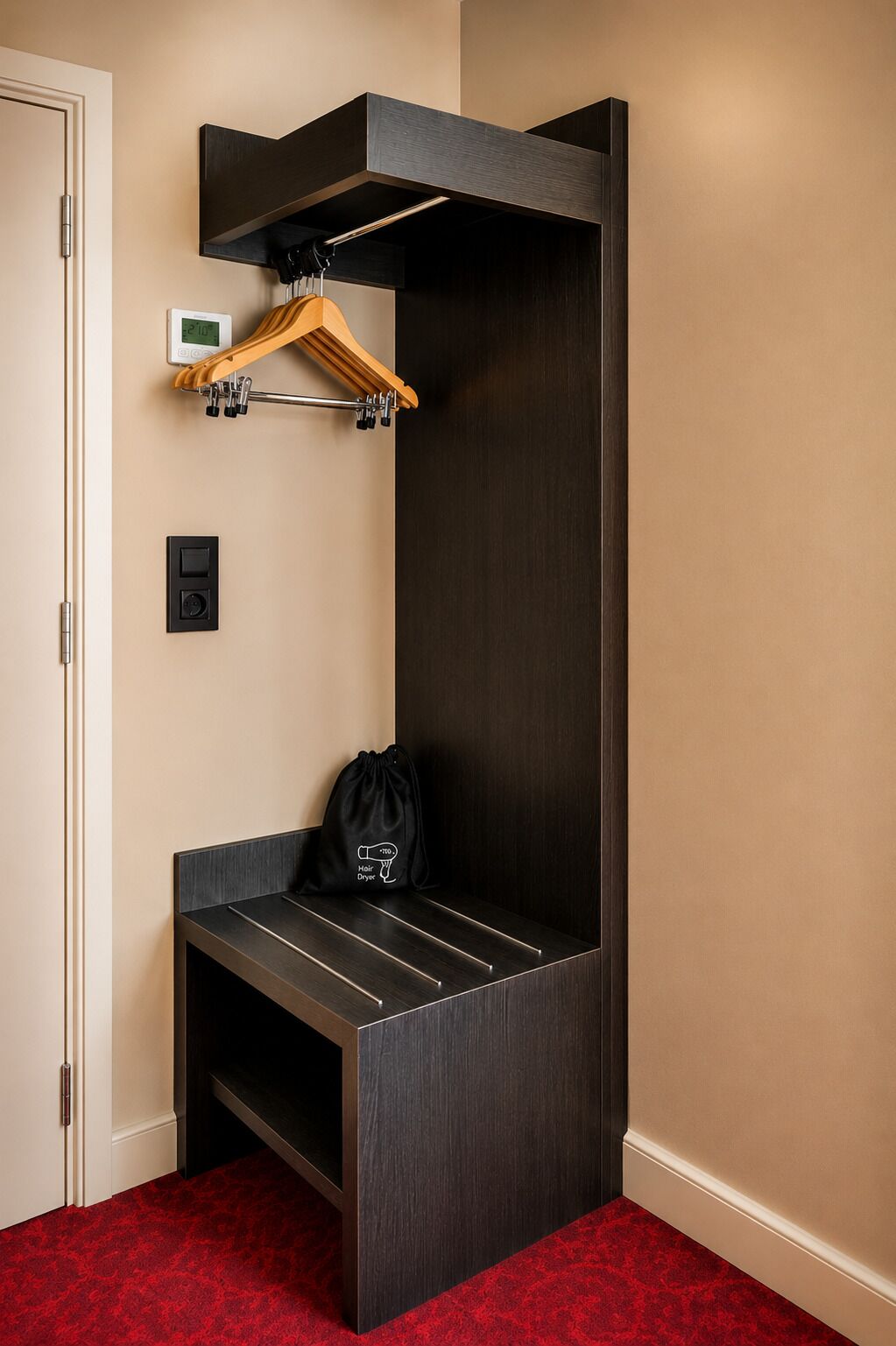 Une pièce d’angle avec un banc en bois foncé, un porte-manteau suspendu, un petit sac noir et une horloge fixée au mur.