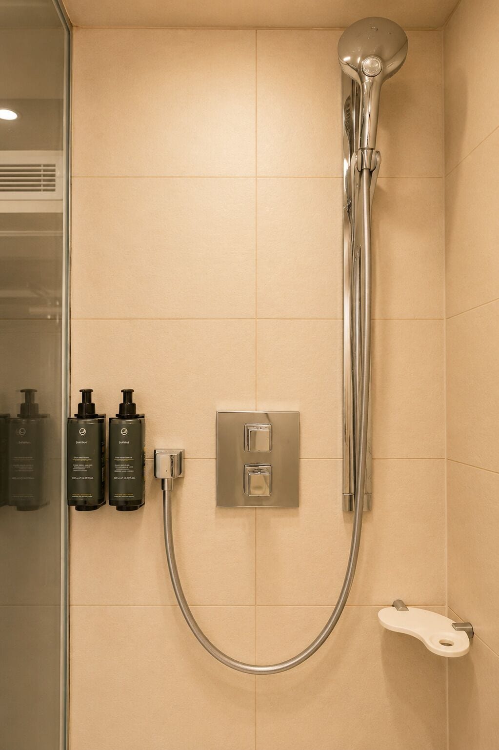 A shower with a handheld showerhead, a wall-mounted control panel, and two bottles of shampoo.