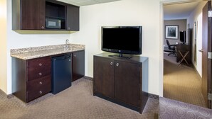 A compact hotel room with a kitchenette, a flat-screen TV, a small desk, and a chair. - Holiday Inn Airport - Portland by IHG (Portland)