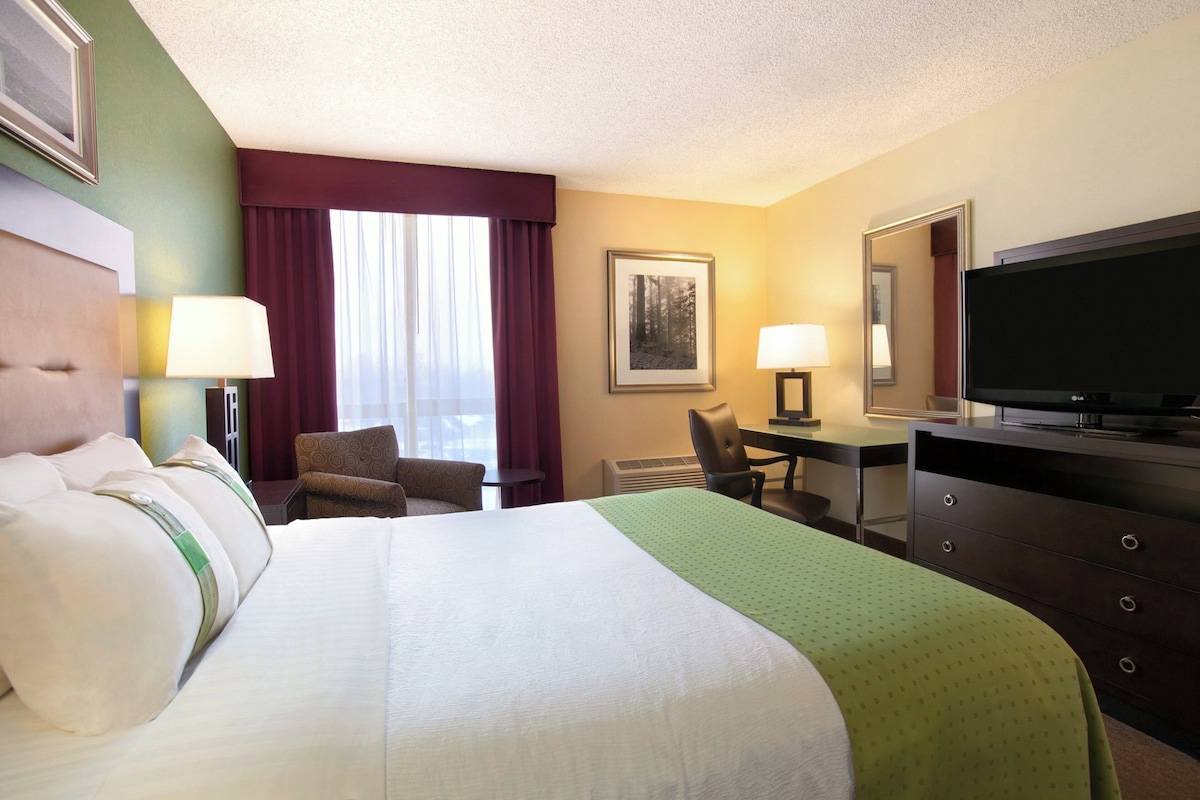 A hotel room with a large bed, a desk, a chair, a television, and a window with curtains.