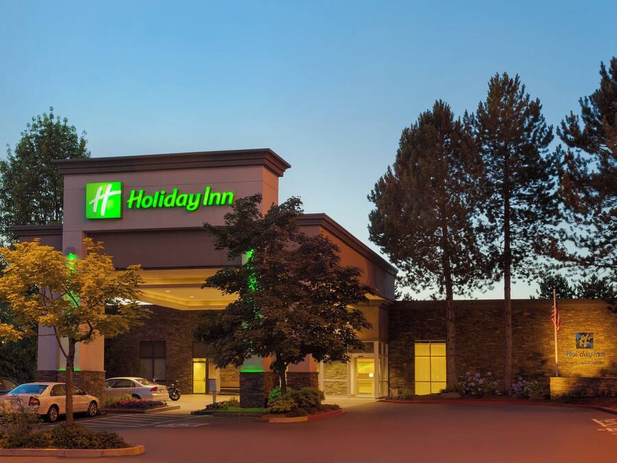 Ein Holiday Inn Hotel mit Ziegelverkleidung, einem sichtbaren Parkplatz und blauem Himmel.