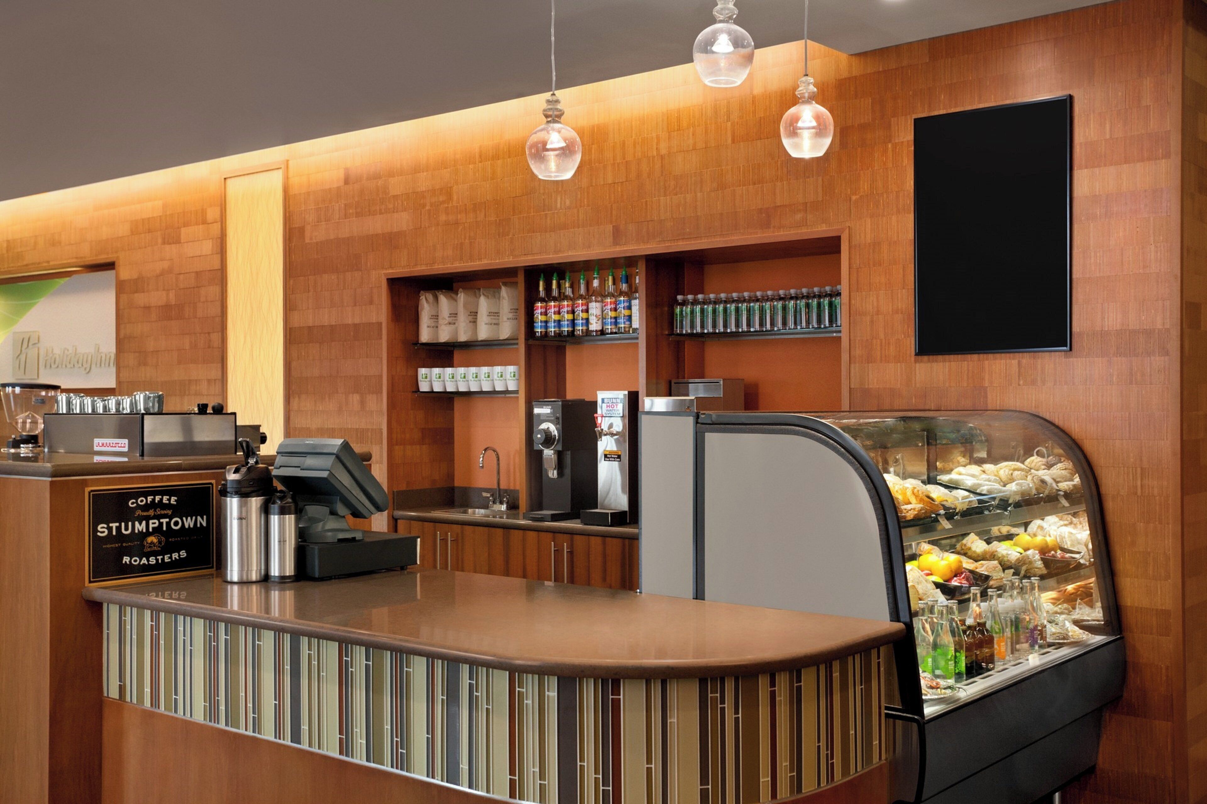 Una estación de café con un letrero de Stumptown Roasters, una máquina de café y una vitrina con pasteles.