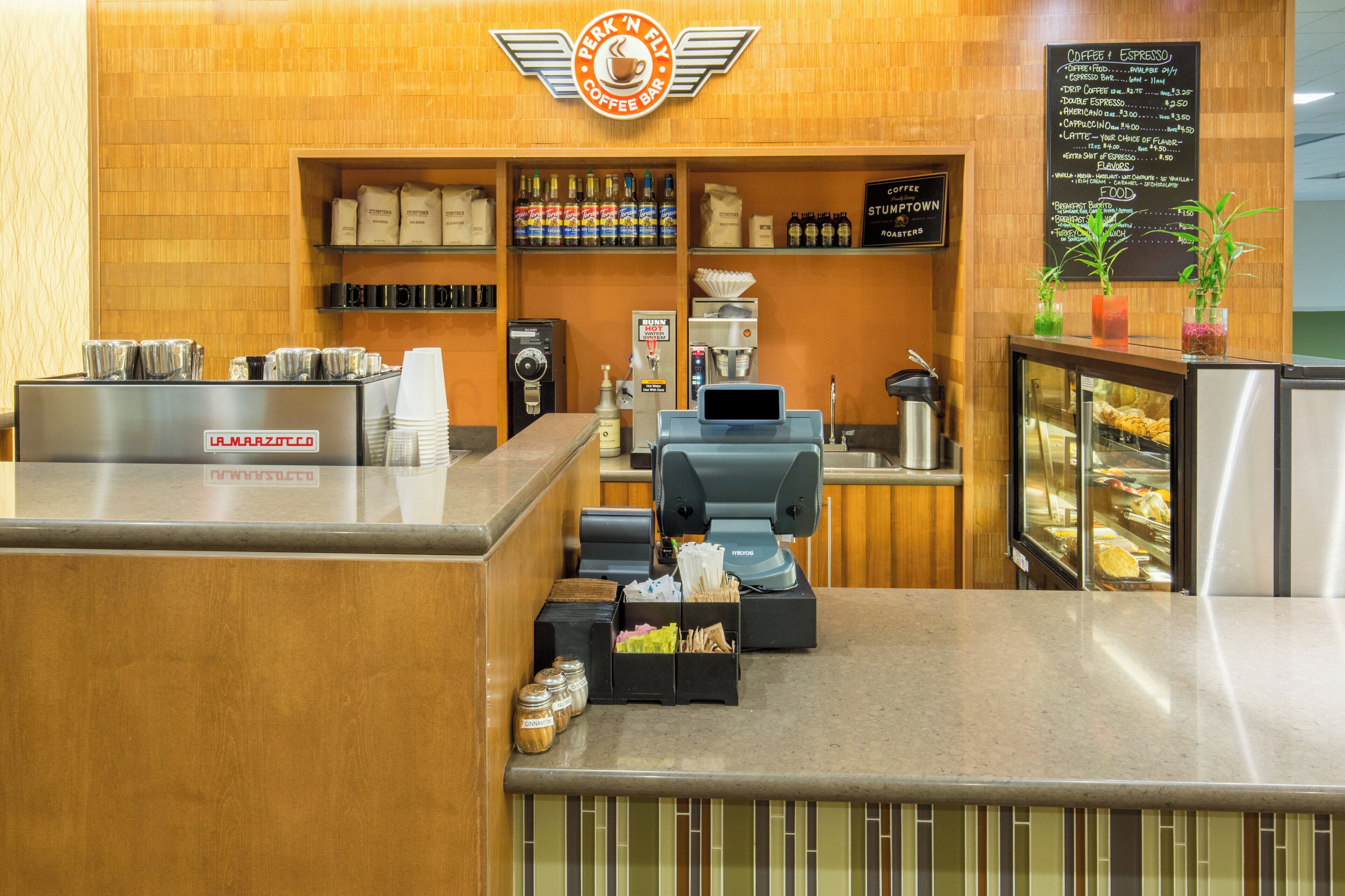 A coffee shop interior with a counter, coffee machines, a menu board, and a display case with pastries.