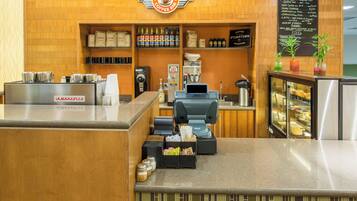 A coffee shop interior with a counter, coffee machines, a menu board, and a display case with pastries.