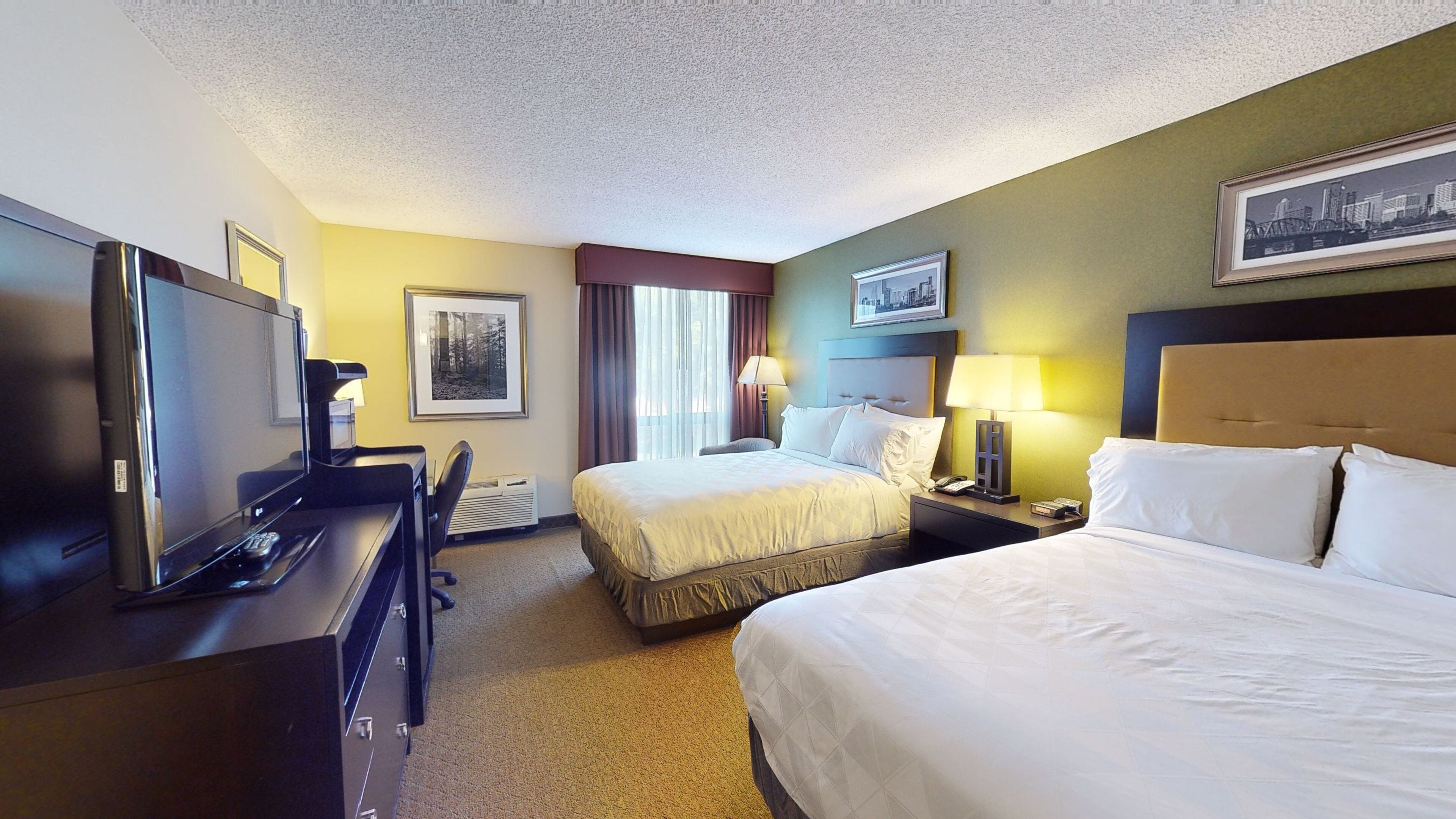 A hotel room with a bed, a desk with a computer, a television, and a framed picture on the wall.