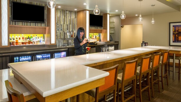A modern bar area with a long counter, multiple bar stools, and a television mounted above the bar. - Holiday Inn Airport - Portland by IHG (Portland)