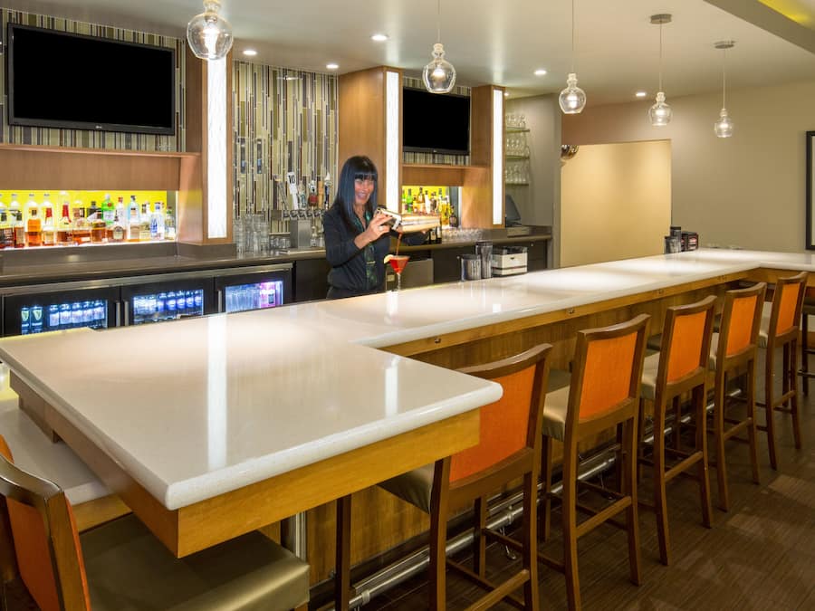 A modern bar area with a long counter, multiple bar stools, and a television mounted above the bar.