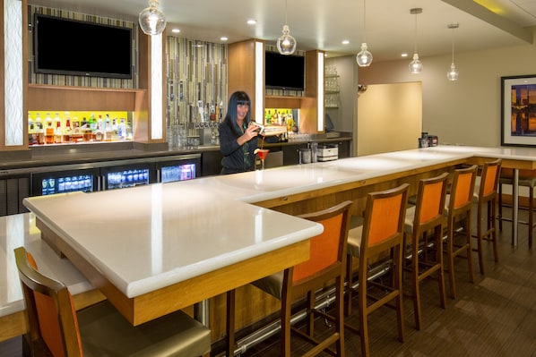 A modern bar area with a long counter, multiple bar stools, and a television mounted above the bar.