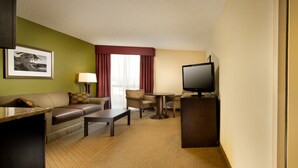A hotel room with a sofa, armchair, coffee table, TV, and a framed picture on the wall. - Holiday Inn Airport - Portland by IHG (Portland)