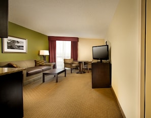 A hotel room with a sofa, armchair, coffee table, TV, and a framed picture on the wall.