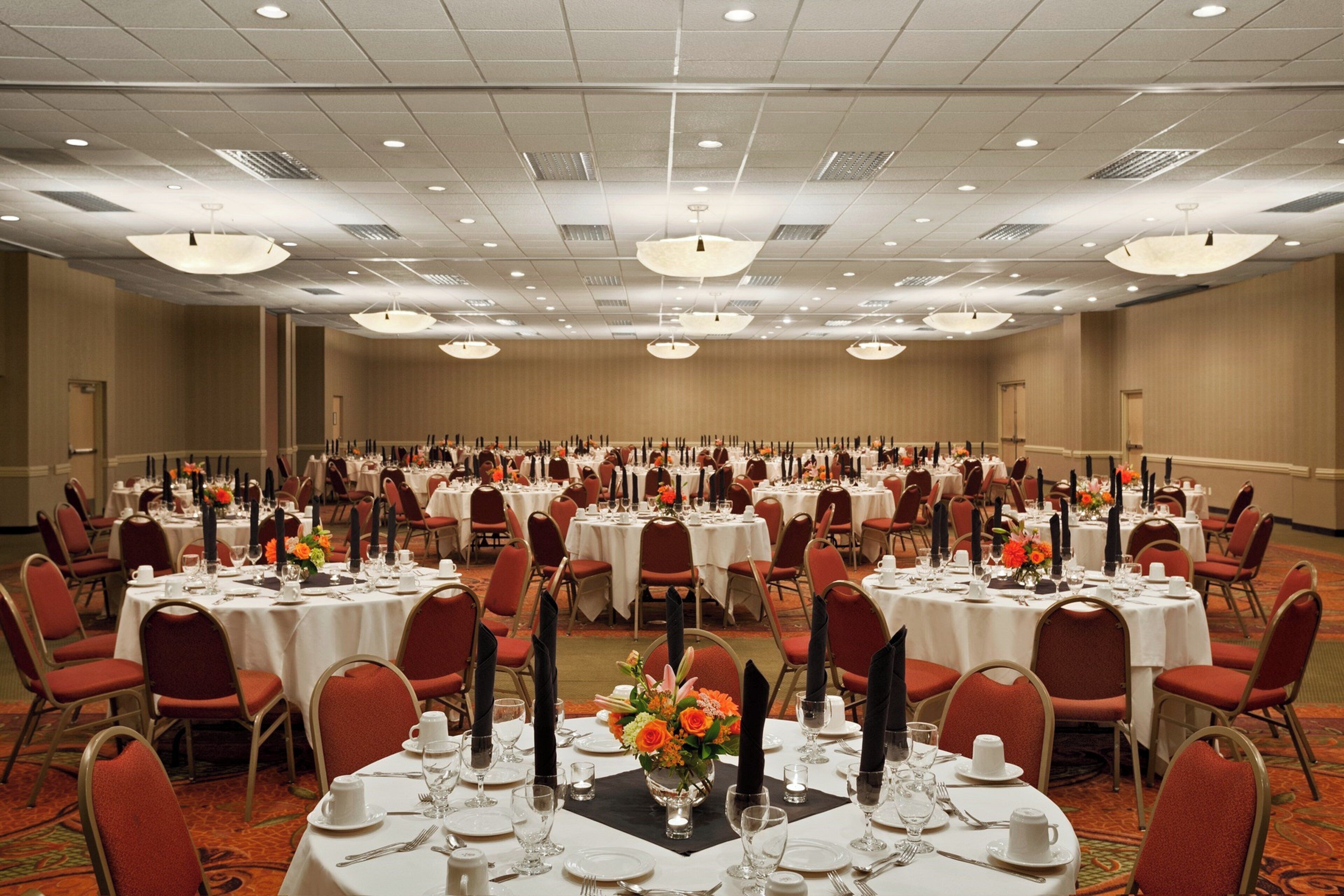 A large banquet hall with multiple round tables set for dining, arranged in rows.