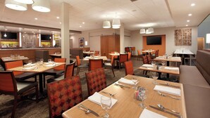 A hotel dining area with multiple tables, chairs, and a bar area.
