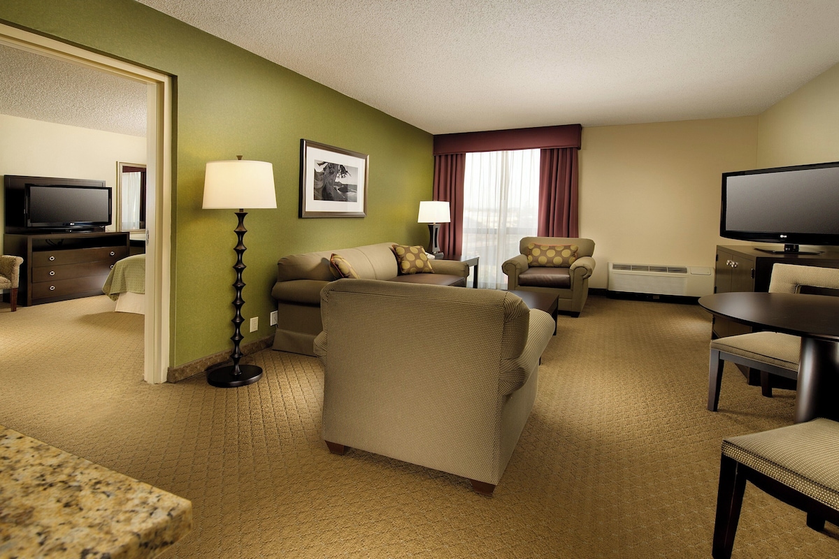 A hotel room with a living area, a dining table, a television, and a sofa.