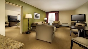 A hotel room with a sofa, armchair, dining table, television, and a lamp. - Holiday Inn Airport - Portland by IHG (Portland)