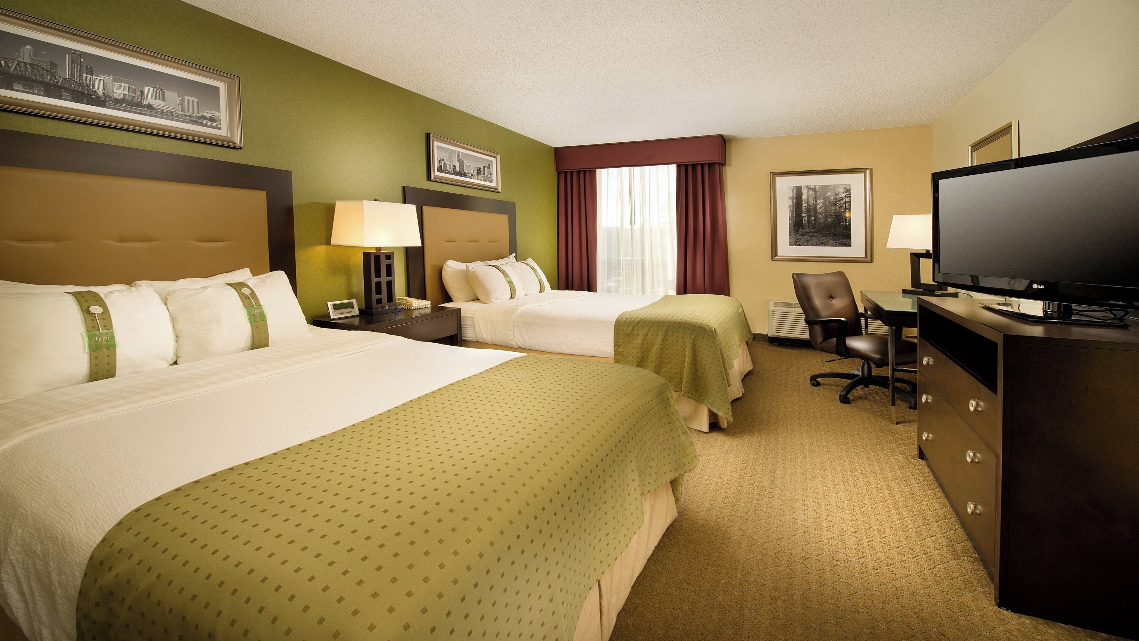 A hotel room with two beds, a desk with a television, and a chair.