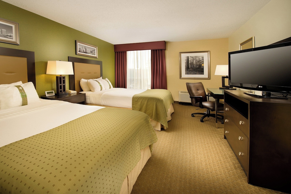 A hotel room with two beds, a desk with a television, and a chair.