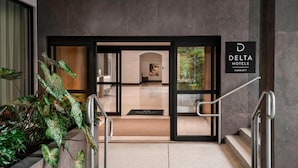 The entrance to a hotel with a modern design, featuring a glass door, a staircase, and a sign indicating it is a Delta Hotels property. - Delta Hotels by Marriott Richmond Downtown (Richmond)