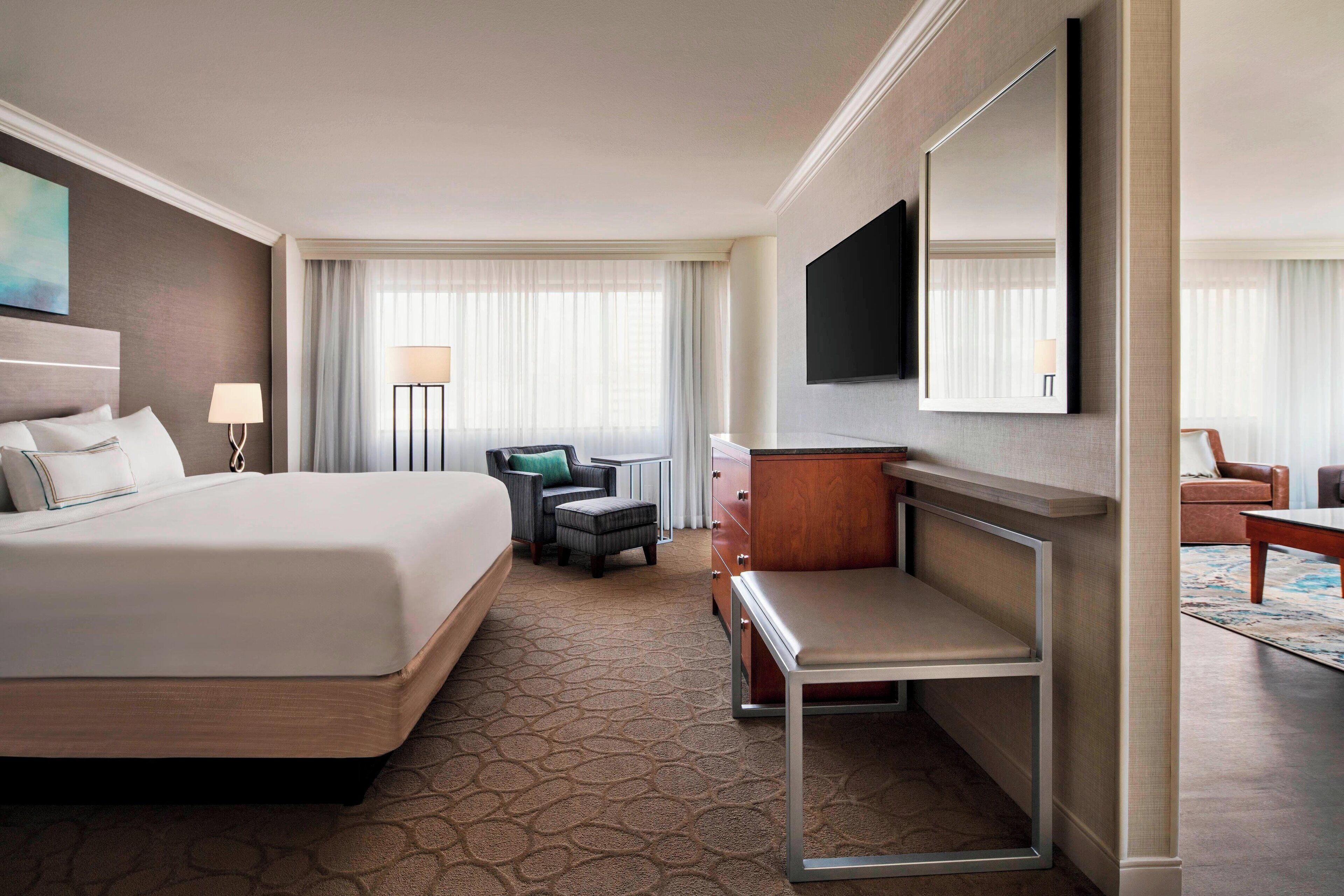 A hotel room with a large bed, a desk, a chair, a TV, and a wardrobe.