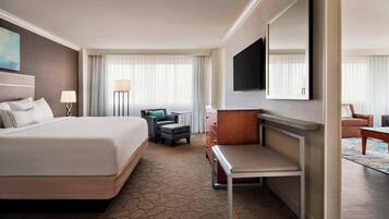 A hotel room with a large bed, a desk, a chair, a TV, and a wardrobe.