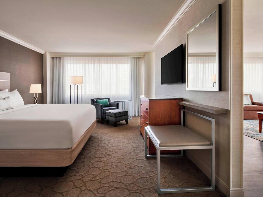 A hotel room with a large bed, a desk, a chair, a TV, and a wardrobe.