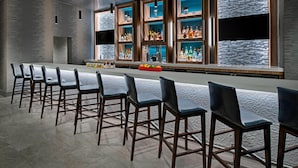 A bar area with a long counter, multiple bar stools, and shelves stocked with bottles. - Delta Hotels by Marriott Richmond Downtown (Richmond)