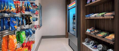 A snack aisle with various bags of chips and snacks, a refrigerated display case, and a beverage dispenser.