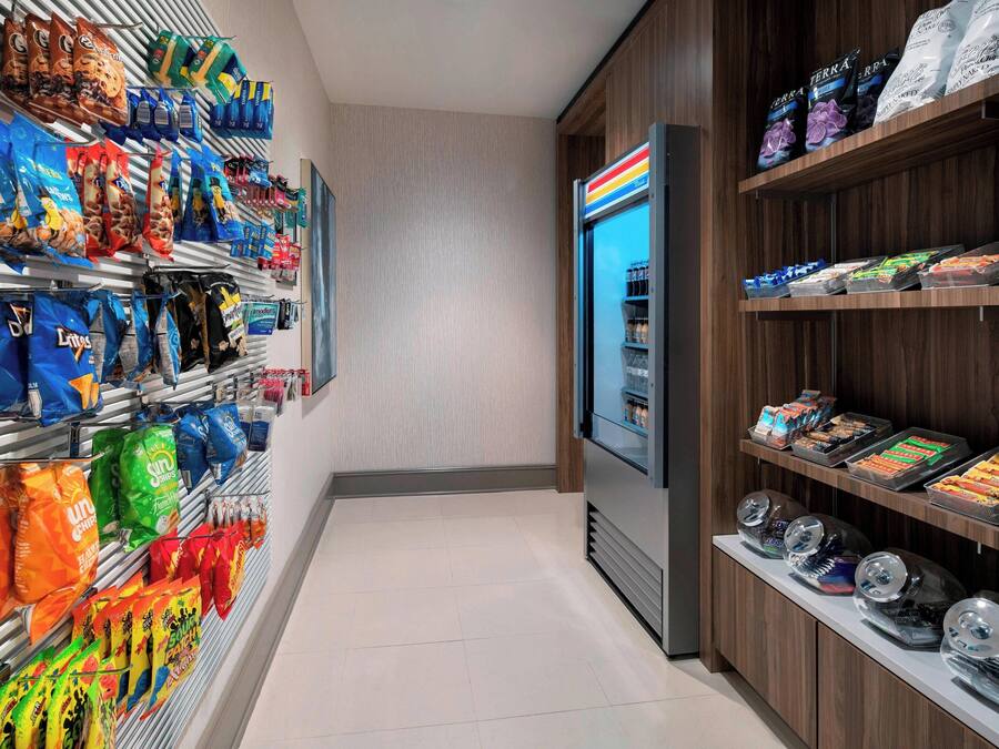 A snack aisle with various bags of chips and snacks, a refrigerated display case, and a beverage dispenser.