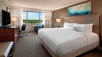 A hotel room with a large bed, a desk with a TV, a chair, a small table, and a view of the outdoors.